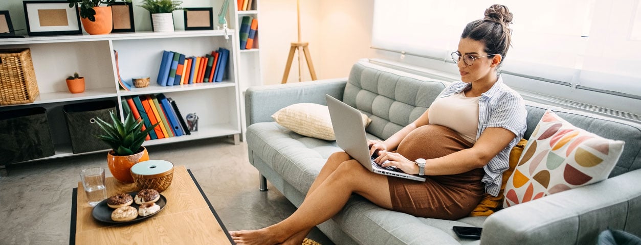 Pregnant woman sitting on a couch using a laptop
