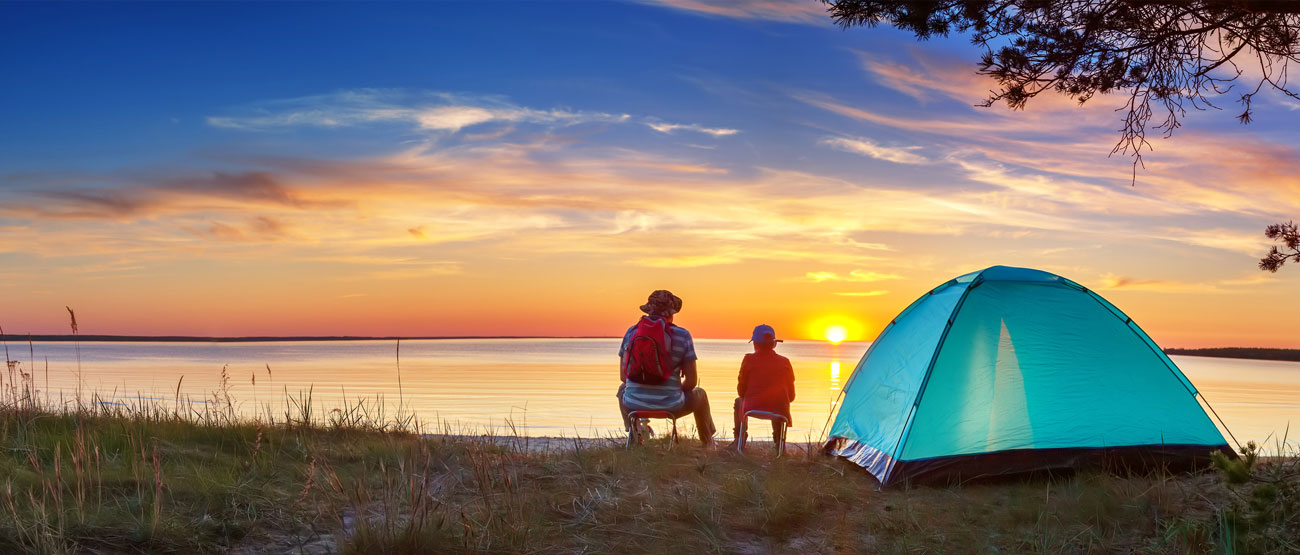 Father and son fishing on the shore near a tent.