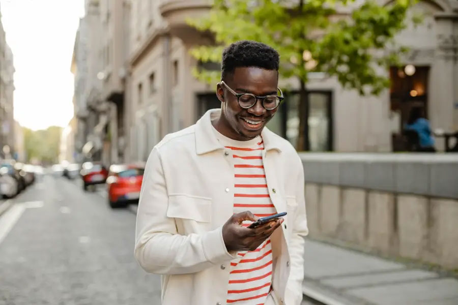 Dark-skinned man standing outside in a city looking at his phone