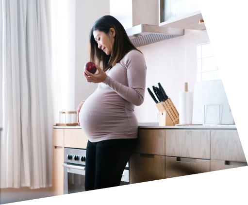 Pregnant woman holding apple standing in kitchen