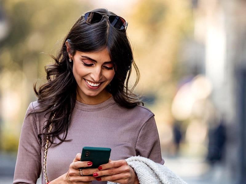 Woman outside smiling looking at her phone